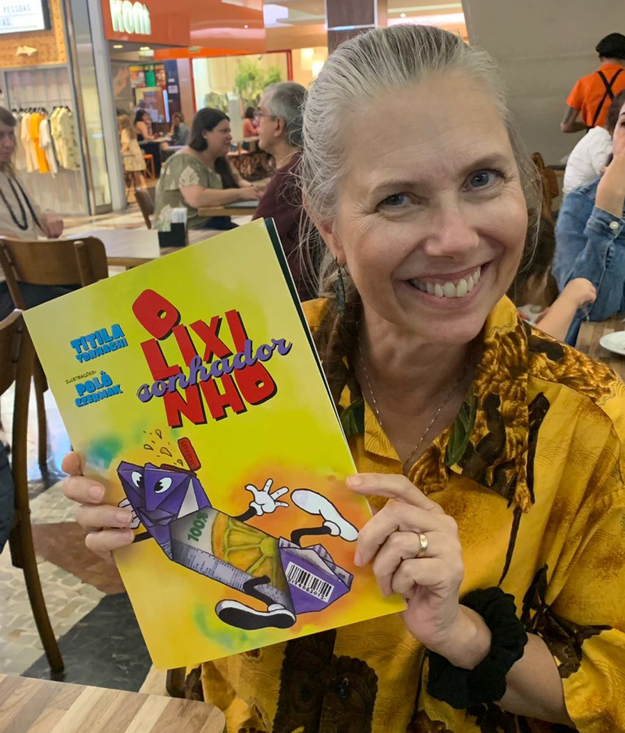 Titila sorri enquanto segura o livro O Lixinho Sonhador